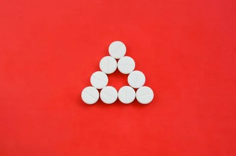 Several white tablets lie on a bright red background in the form of an even t Stock Photos