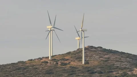 Several wind turbines rotating on a rocky, shrub-covered hill in Opoul Perillos Stock Footage 346697716