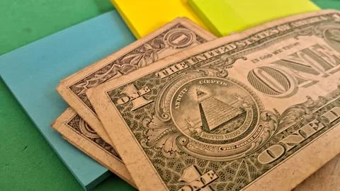 Several worn one dollar bills resting on colorful adhesive note pads Stock Photos