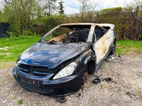 Severely burned black car with missing wheels and extensive fire damage, aban Stock Photos
