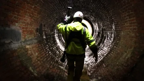 A sewer district worker leads the path with a light down an old 動画素材 108148584