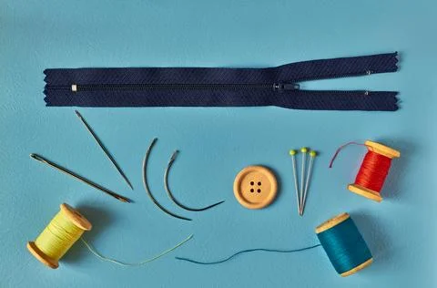 Sewing accessories - needles, thread, pins, and zipper on blue background Stock Photos