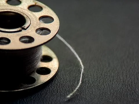 A sewing bobbin with white thread presents an intriguing visual narrative, .. Stock Photos