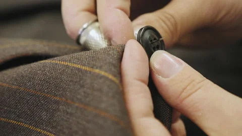 Sewing a button onto a brown jacket tailored suit, closeup Stock Footage 130242653