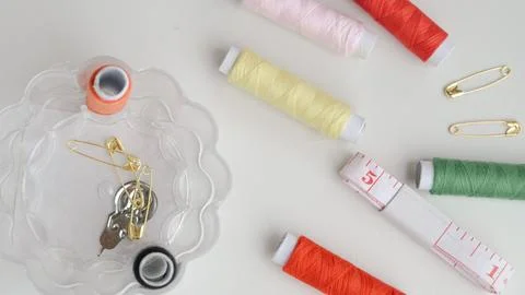Sewing composition with threads, pins, and tape on neutral white surface Stock Photos