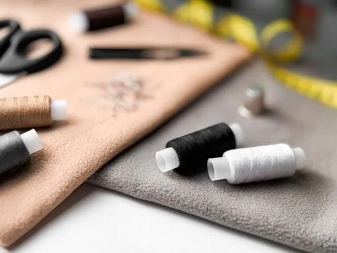 Sewing essentials with thread spools, needles, and measuring tape on fabric Stock Photos