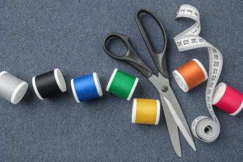 Sewing items: tailoring scissors, measuring tape, spools of threads. Stock Photos