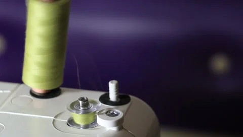 Sewing machine bobbin winding activity. Light green thread spool unwinding as Stock Footage 329621674