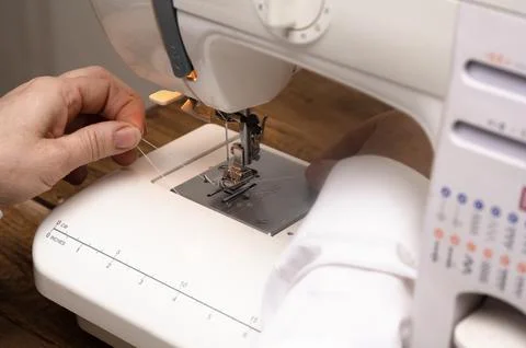 Sewing machine closeup with hands threading needle before stitching begins. Stock Photos