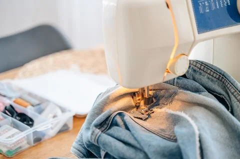 Sewing machine foot stitching denim fabric with warm light, tailoring detai.. Stock Photos