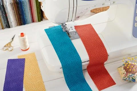 Sewing machine with a strips of fabrics on the background of stack of color.. Stock-Fotos