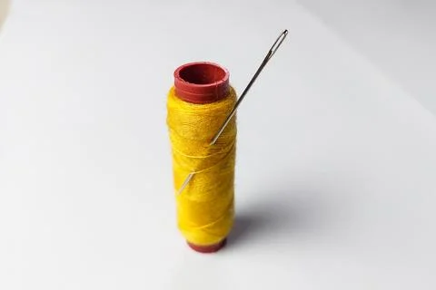 Sewing needle stuck in yellow thread on white background Stock Photos