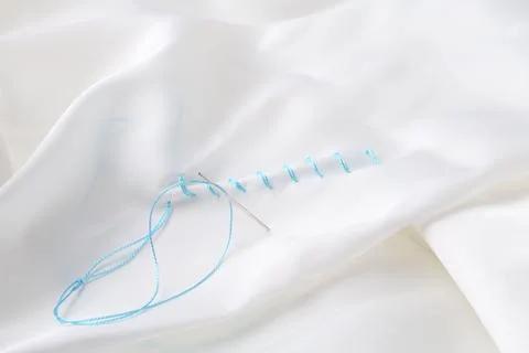 Sewing needle with thread and stitches on white cloth, closeup Stock Photos