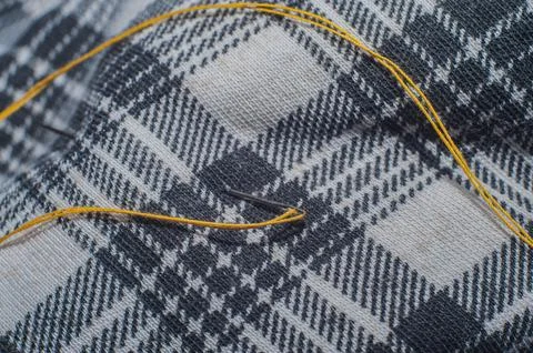 Sewing needle with thread stuck in a checkered fabric. Stock Photos