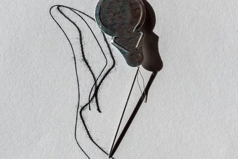 Sewing needle threader tool in use and a single black string. Foto stock