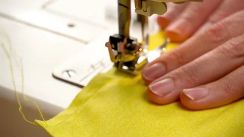 Sewing process, female hands feed yellow fabric under the sewing machine foot. Stock Footage 143584305
