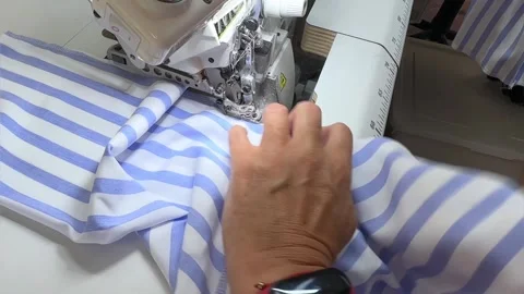 The sewing process. The hand gently passes the blue and white striped fabric Stock Footage 296074566