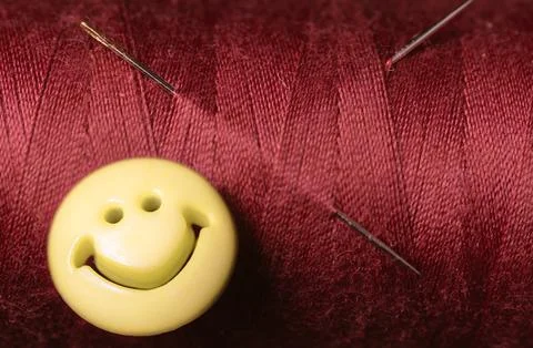 Sewing red thread and sewing needle withe a yellow smile button.selective foc Stock Photos