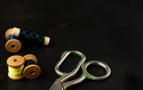 Sewing scissors and thread spools on black background Stock Photos