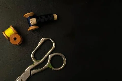 Sewing scissors with thread spools on dark surface Stock Photos