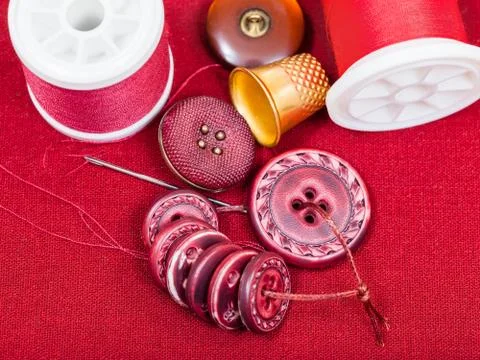 Sewing thread, buttons, thimble on red textile Stock Photos