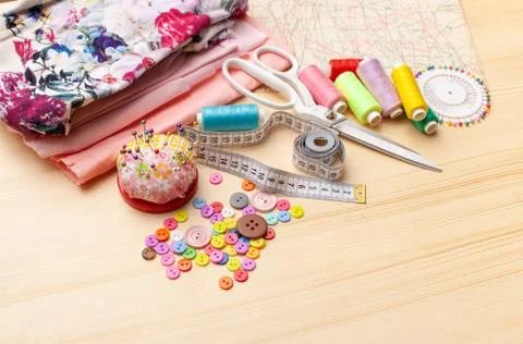 Sewing thread, spool of thread, pieces of cloth, buttons on wooden table Stock Photos