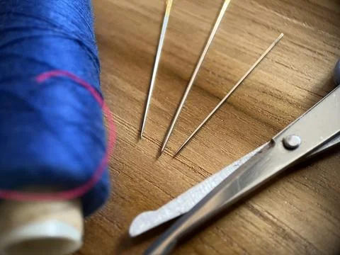 Sewing tool featuring cotton thread, needle and scissor with wood background Stock Photos