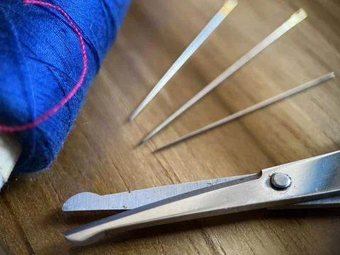 Sewing tool featuring cotton thread, needle and scissor with wood background Stock Photos