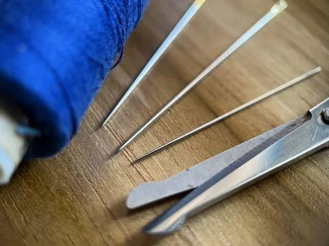 Sewing tool featuring cotton thread, needle and scissor with wood background Stock Photos