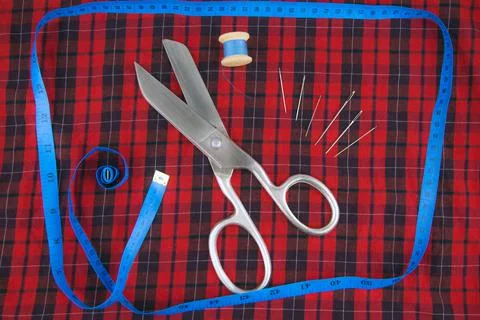 Sewing tools: large scissors and thread with needles lying on a checkered red Stock Photos