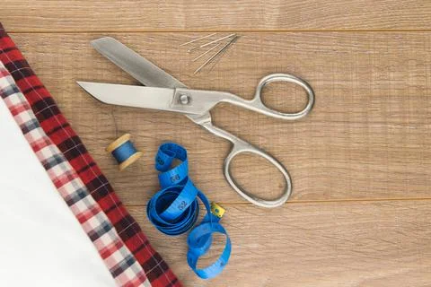 Sewing tools: large scissors, measuring tape, spool of thread and needles lie Stock Photos