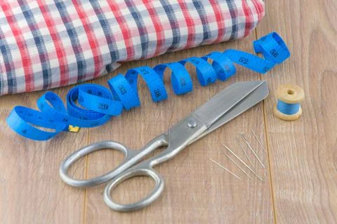 Sewing tools: large scissors, measuring tape, spool of thread and needles lie Stock Photos