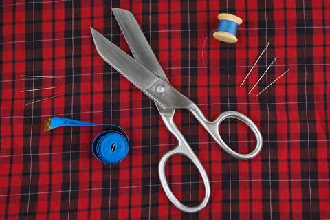 Sewing tools: large scissors, meter and thread with needles lying on a checke Foto stock
