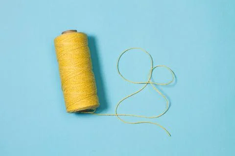 Sewing yellow thread spool on a light blue background Stock Photos