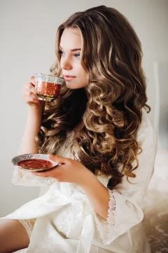Sexy bride in a white robe drinking tea. Wavy hair, wound, makeup bright wedding Stock Photos