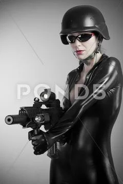 Sexy brunette woman in latex jumpsuit with heavy gun and helmet Stock Photos