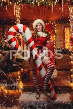 Sexy Santa girl in red body suit and striped stockings holds a big lollipop a Stock Photos
