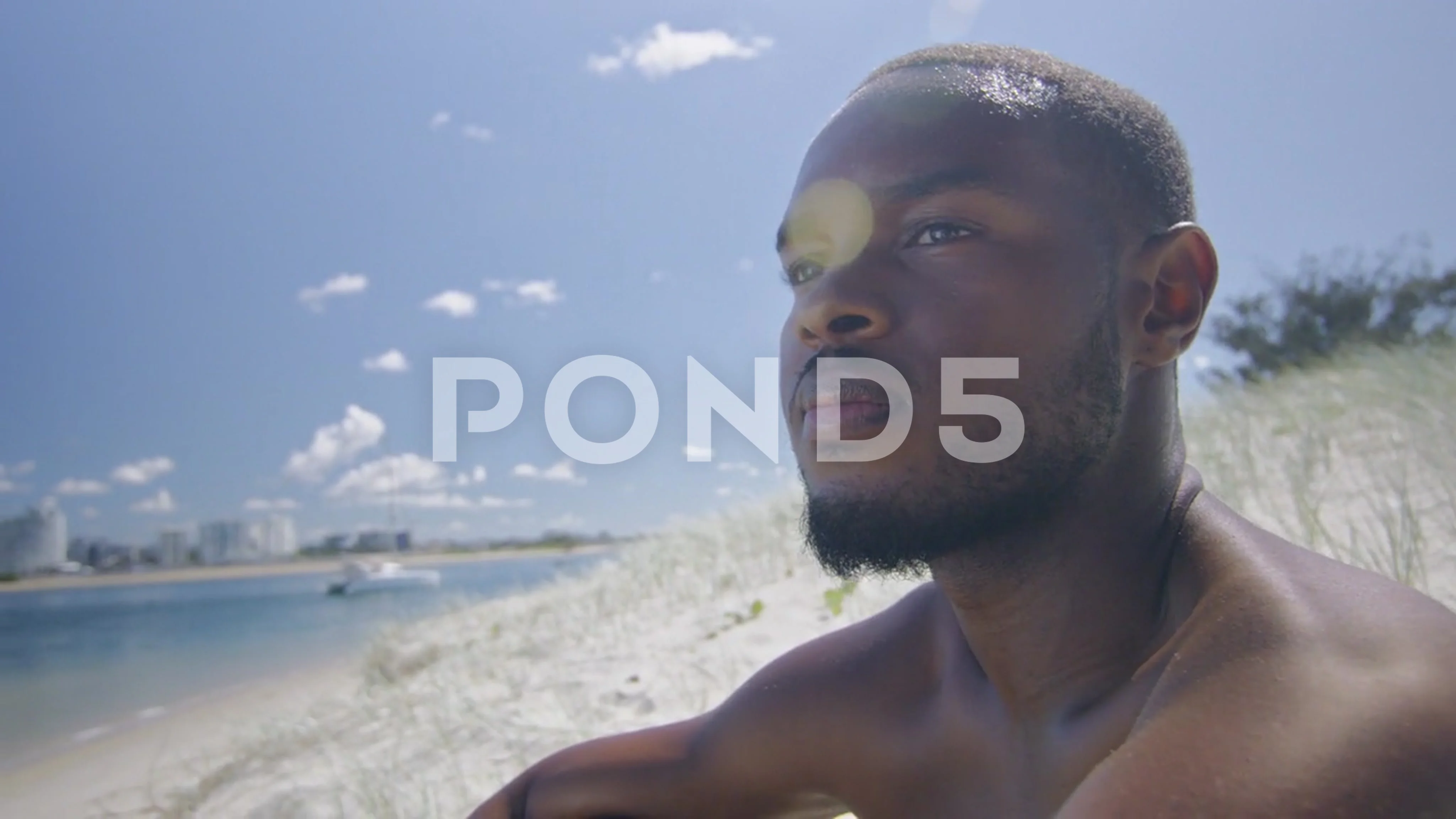 Sexy shirtless black man sits on beach under sunny blue sky in Australia.  Medium