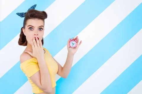 Sexy surprised woman with alarm clock in hands and open mouth. Colorful backg Stock Photos