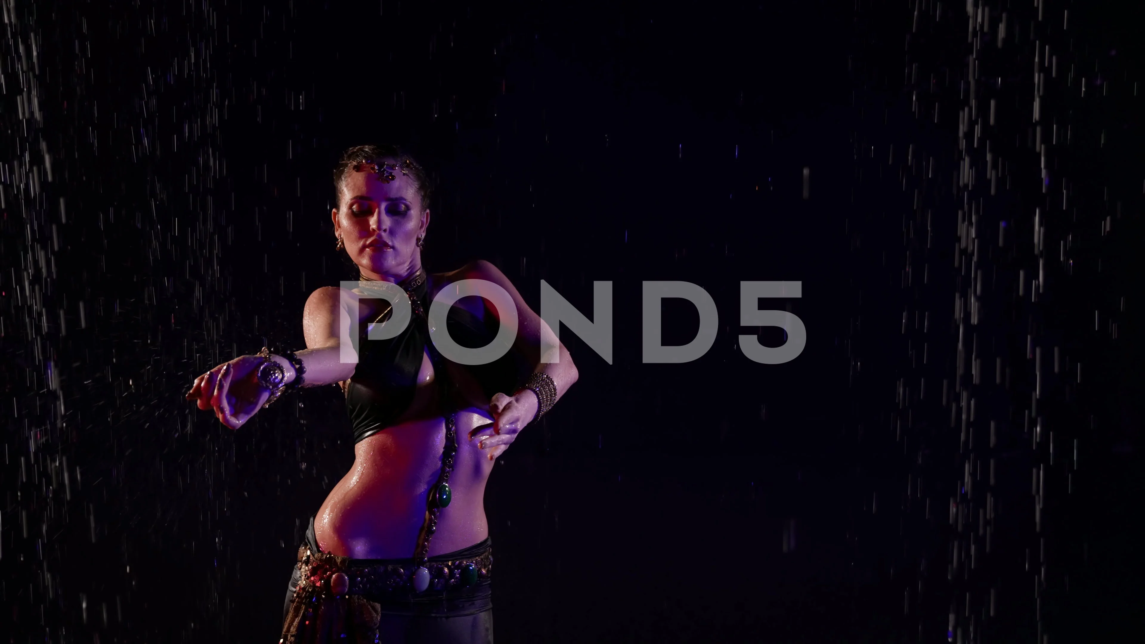 sexy woman is dancing belly dance in darkness, standing under water flows