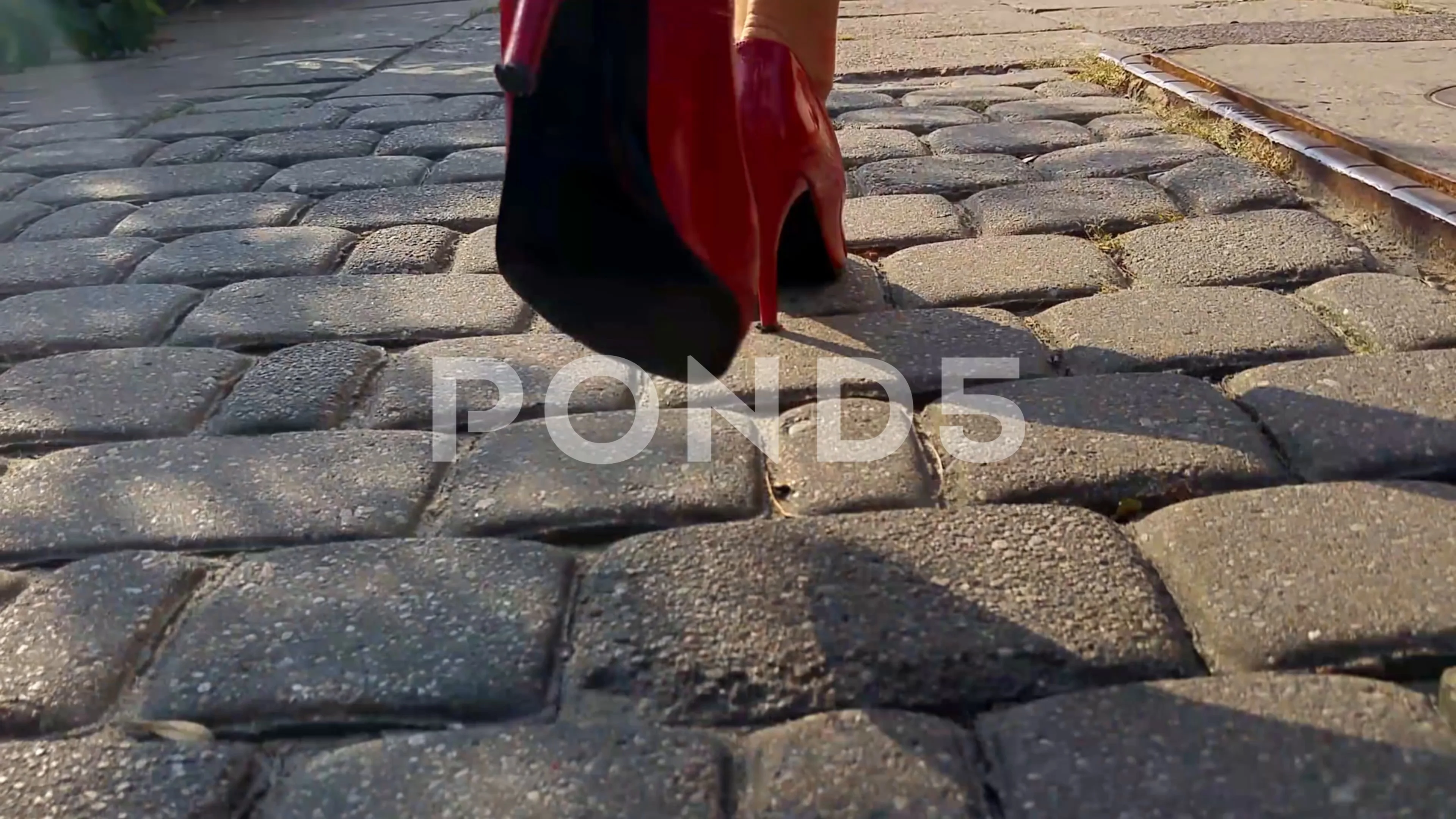 Photo of Closeup of sexy woman legs in high heel shoes and red dress  walking on cobbled city street