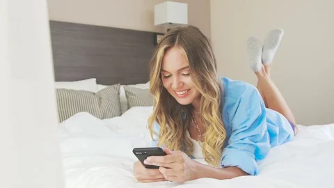 Sexy woman in a shirt lies on a bed, kicking feet and dreaming Stock Footage