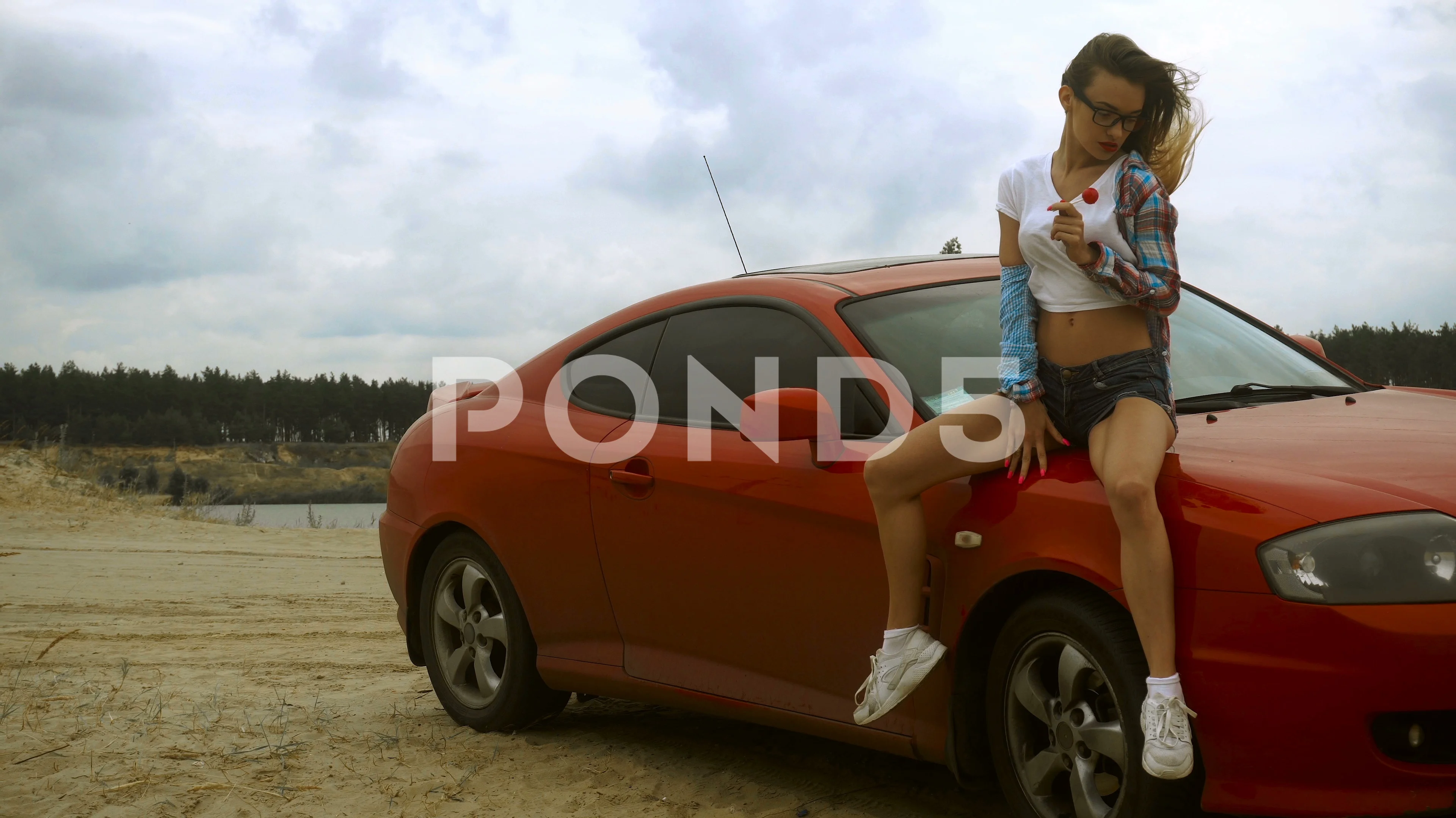 Sexy young blonde sits on a red car and licks a lollipop