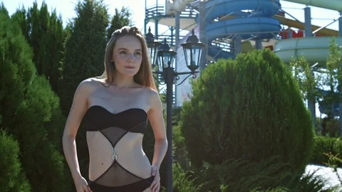 Sexy young woman in bathing suit posing while standing in greenery in water park Stock Footage