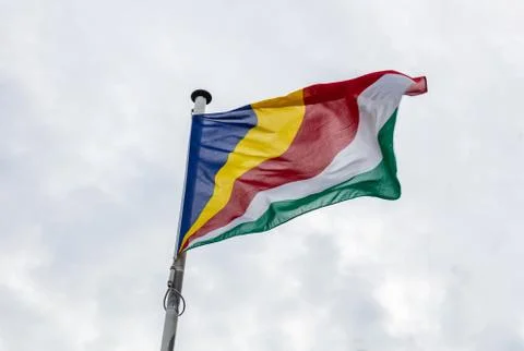Seychelles flag on a pole waving on cloudy sky background Stock Photos