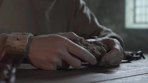 Shackled prisoner tearing a large loaf chunk of bread inside a gloomy cell Stock Footage 339630997
