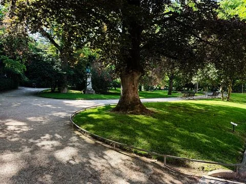 Shaded park path with large tree, benches and statue in a quiet Luxembourg .. 库存照片