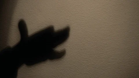 Shadow of arm on white wall making figure of barking dog Vidéo 102627605