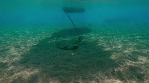 In shadow of boat, an anchor lies on sandy bottom in shallow water, backlit Stock Footage 327620197