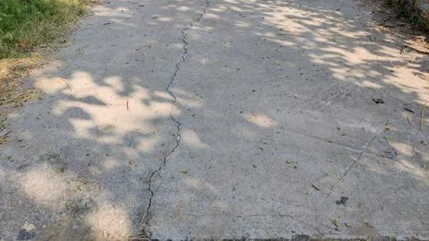 Shadow cast across cracked cement road showing urban wear and surface decay Stock Photos
